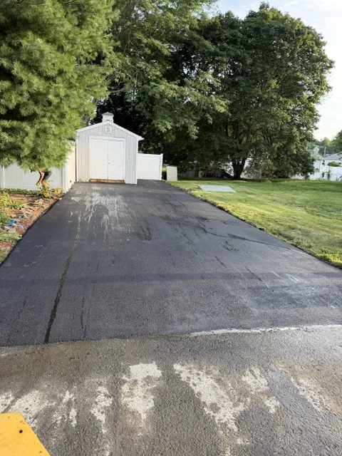 Wide resurfaced asphalt pad leading to a white storage shed
