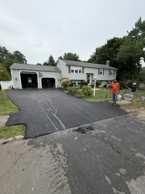 Crew finishing a new asphalt driveway at a split-level home