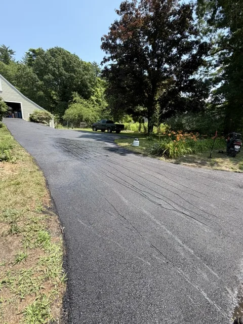 Long freshly paved private drive curving past trees toward a barn